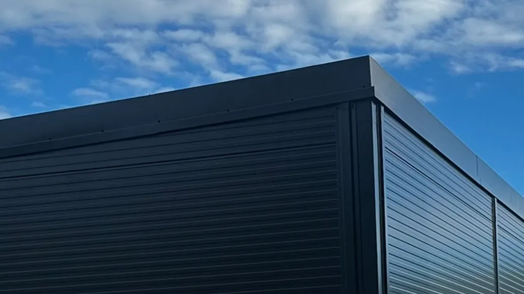 Ferdig konstruksjon kledd med mørke sandwichelementer, sikret på trailer under blå himmel